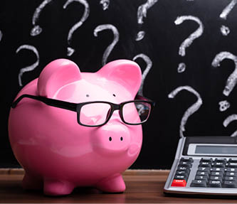Close-up Of A Pink Piggybank With Eyeglasses And Calculator On Wooden Desk