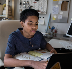 African American teenage boy uses laptop while studying for a biology test  A biology textbook is in front of him 