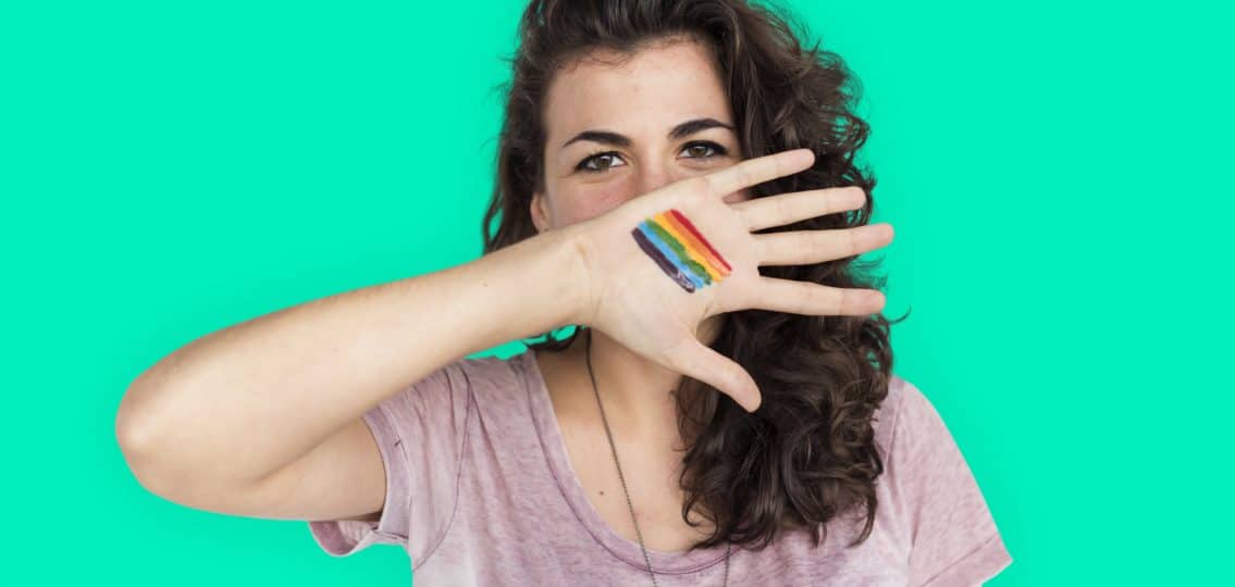 smiling teenage girl covering her face with an open hand with a rainbow gay pride parade on her palm