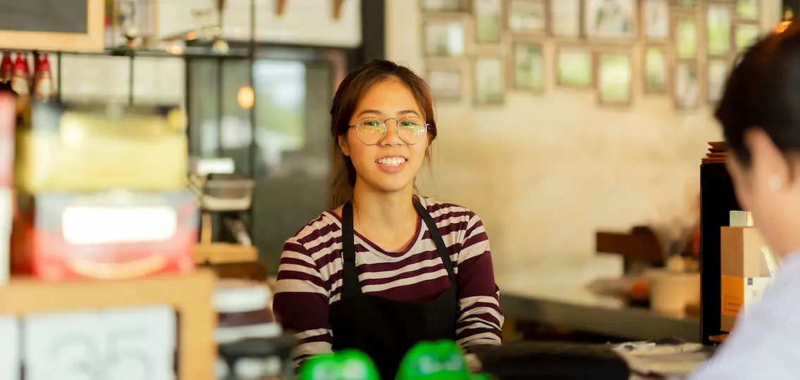 Young woman barista serving customer with smile face at counter bar in cafe