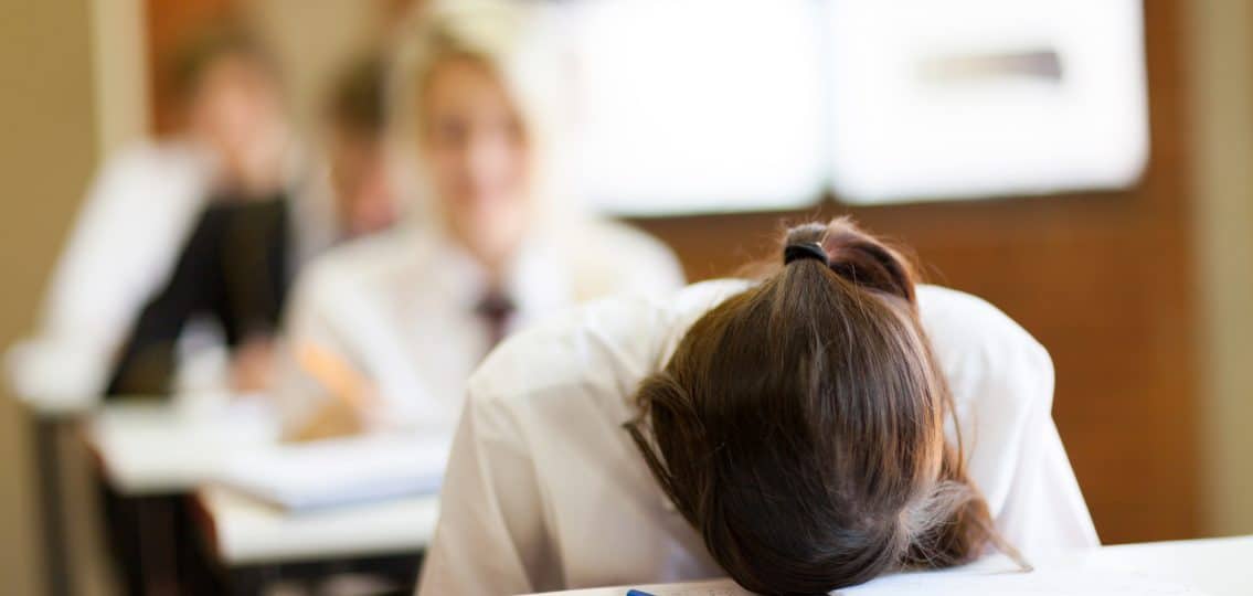 frustrated high school student in classroom with her face lying on her homework