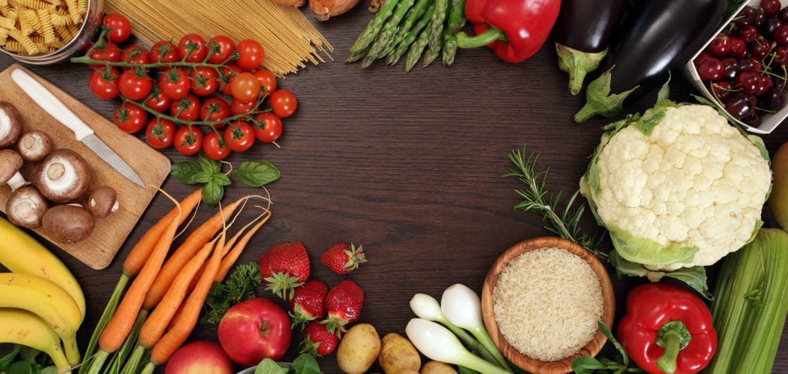 Photo of a table top full of fresh vegetables, fruit, and other healthy foods with a space in the middle