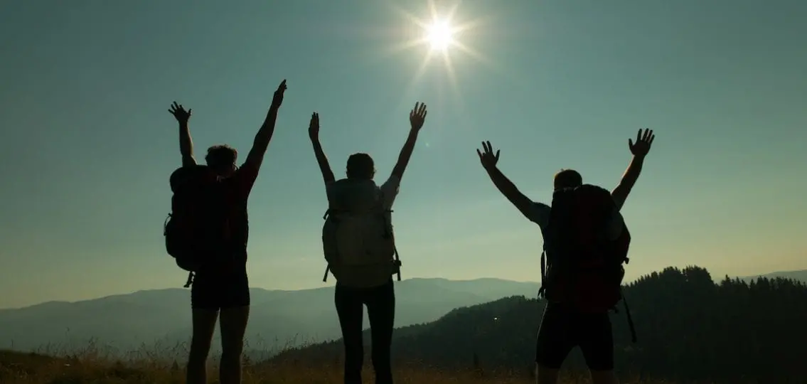 three cheering silhouettes on a mountain in hiking gear