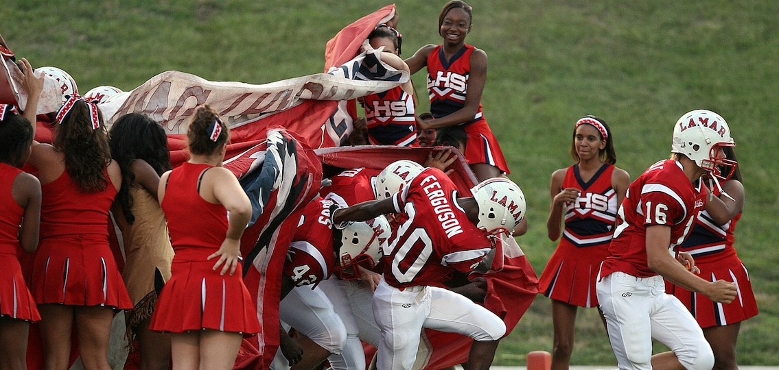 High school football game football players running past cheerleaders