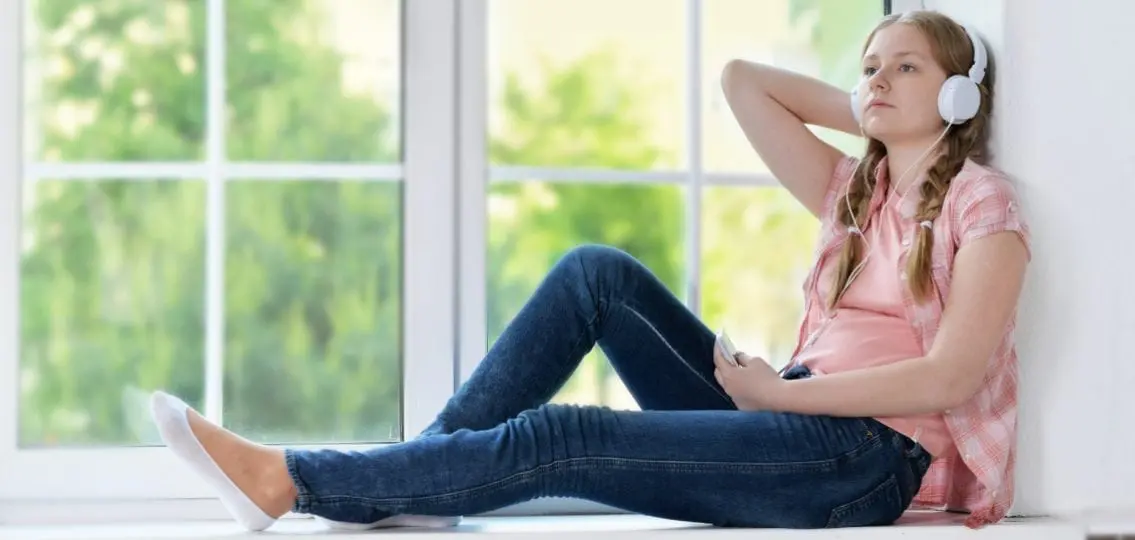 young teen girl in a windowsill relaxing in headphones at home