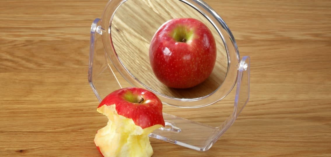 Metaphor for anorexia or bulimia eating disorder, apple in front of a mirror