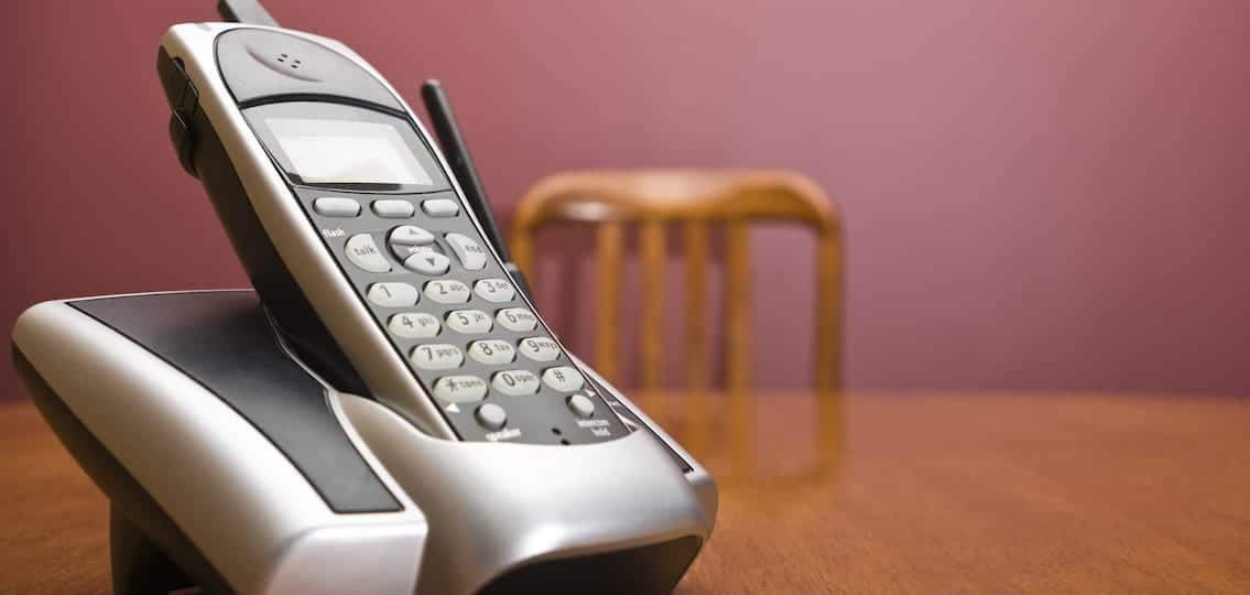 A cordless phone on a table with an out of focus chair