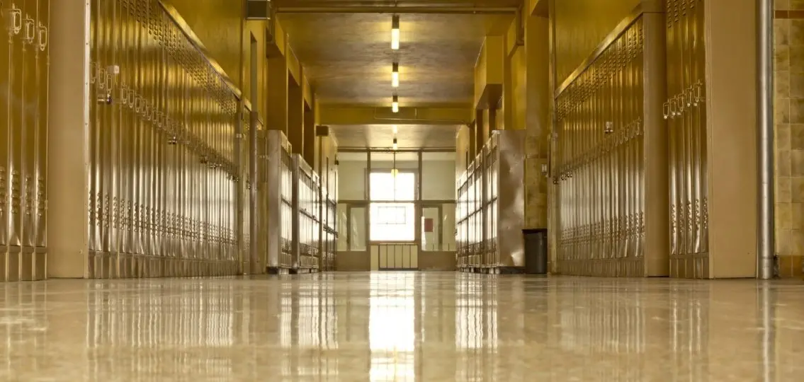 An empty high school corridor with a bright light at the end of the hallway