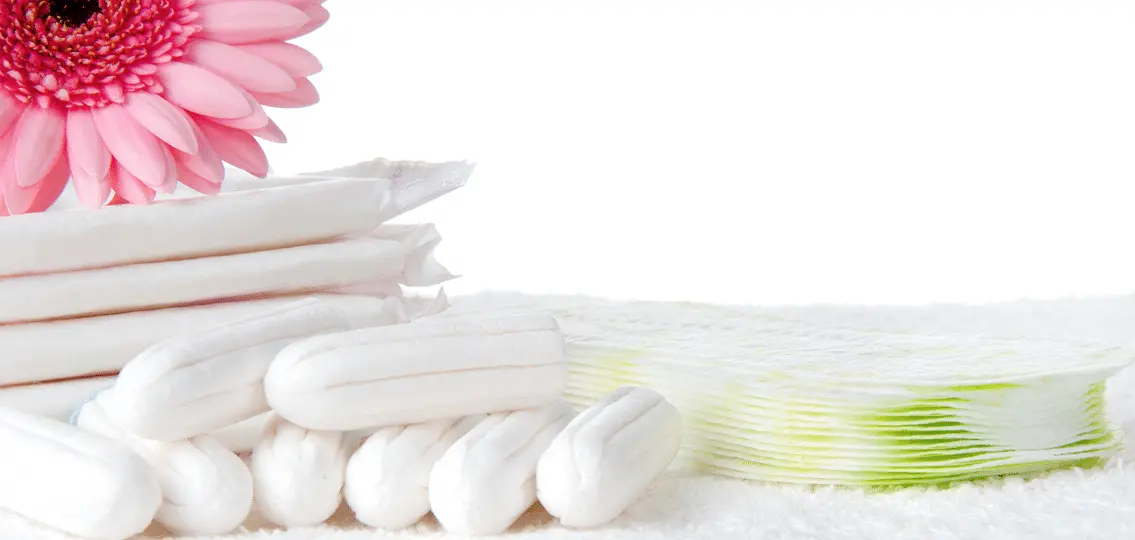 pile of pads and tampons on a white bath rug with a pink flower
