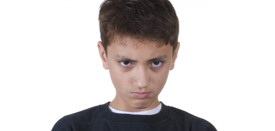 surly 13-year-old boy glaring at the camera white background