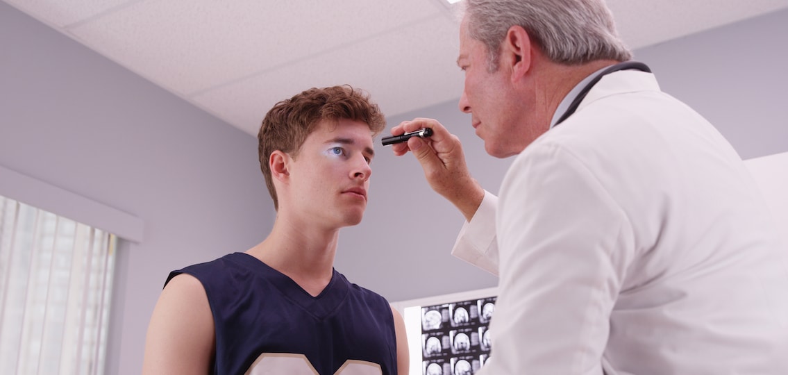 Senior medical doctor checking basketball player's eyes with flashlight.
