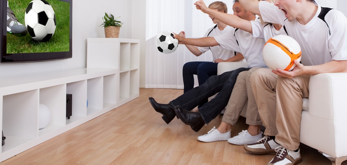 Family watching soccer television as they cheer holding soccer balls and wearing jerseys