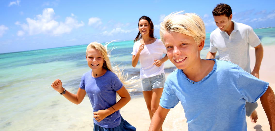 Cheerful family running on a sandy beach mom dad and two young teens