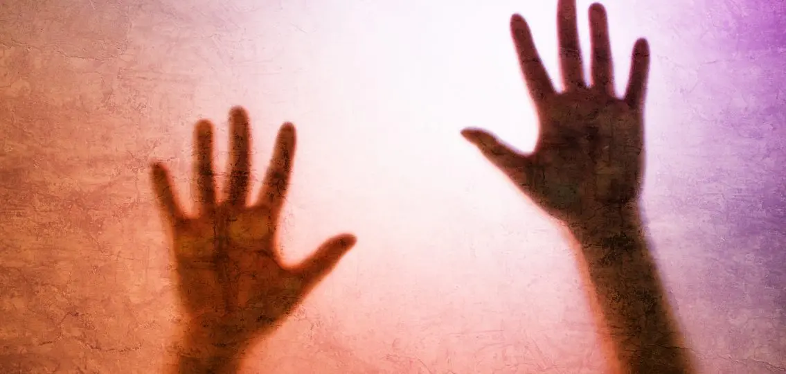 Captured female person concept with back lit silhouette of hands behind matte glass, useful as illustrative image for human trafficking, prostitution, imprisonment, mental illness, depression.