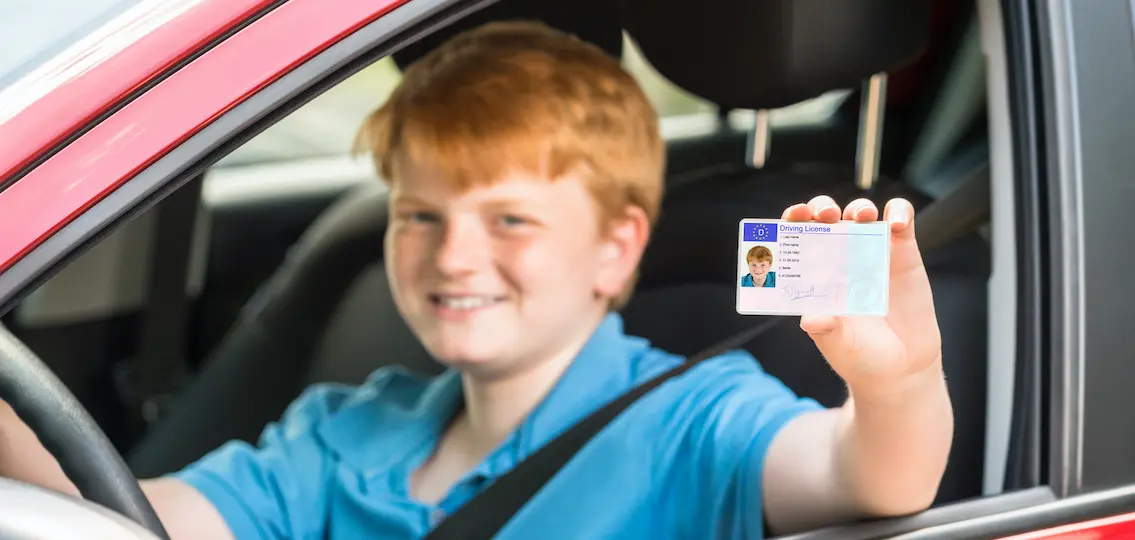 Smiling Boy Sitting Inside Car Showing Driving License