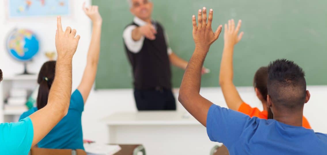 group of students with hands up in classroom during a lesson