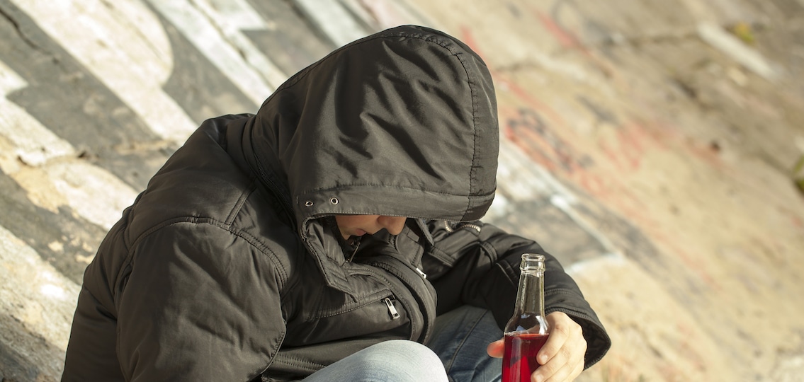 Young middle school teen drinking alcohol in a coat outside
