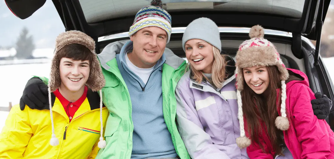 family vacation with teens in winter gear at back of minivan