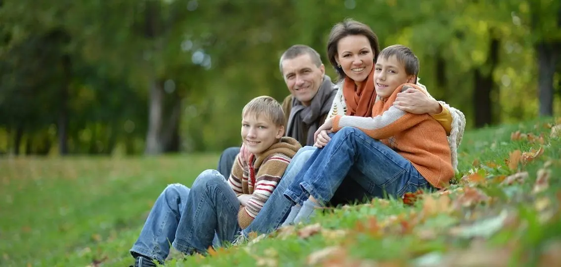 family sitting on a grassy hill with two teen boys smiling at camera