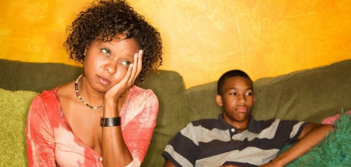 annoyed mom with head in hands next to slumped teen boy on couch