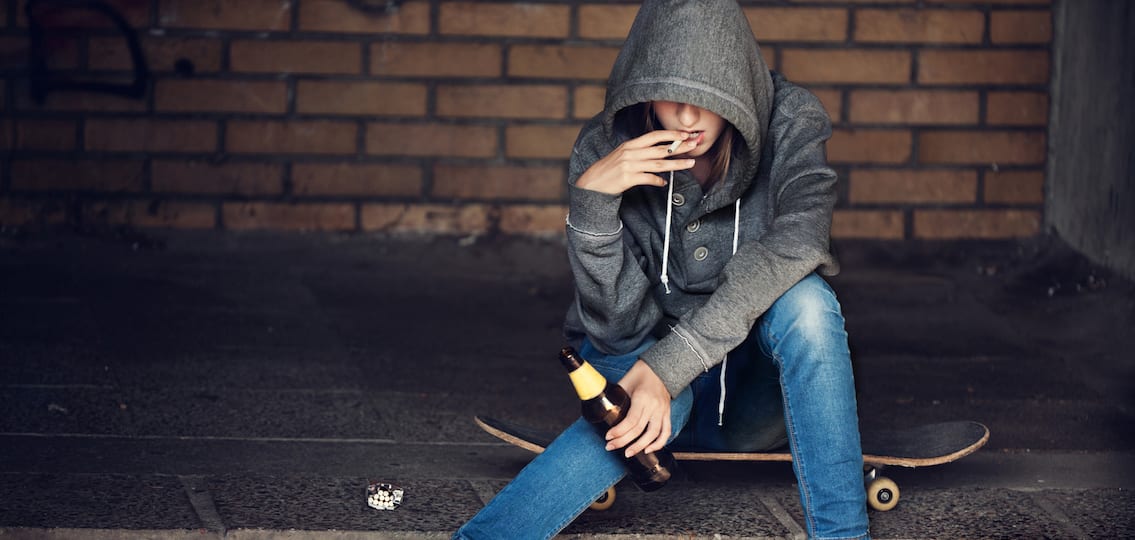 Teen Girl in a hoodie Holding A Beer Bottle And Smoking on a skateboard