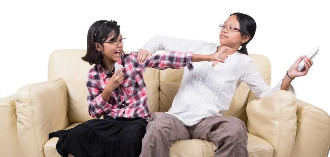 teen sisters fighting over a remote on the couch