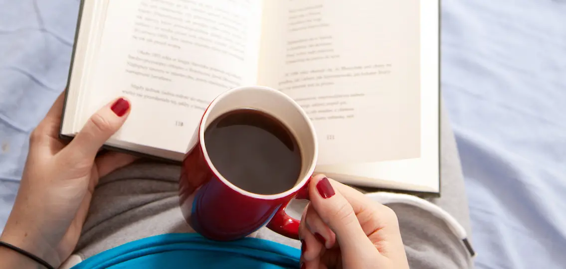 Woman reading a book in bed with coffee