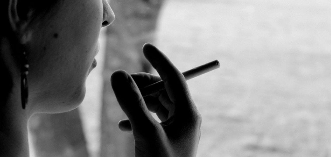 black and white image of a girl smoking a cigarette looking away from the camera