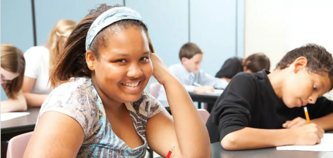 middle school girl smiling in class while other work on homework