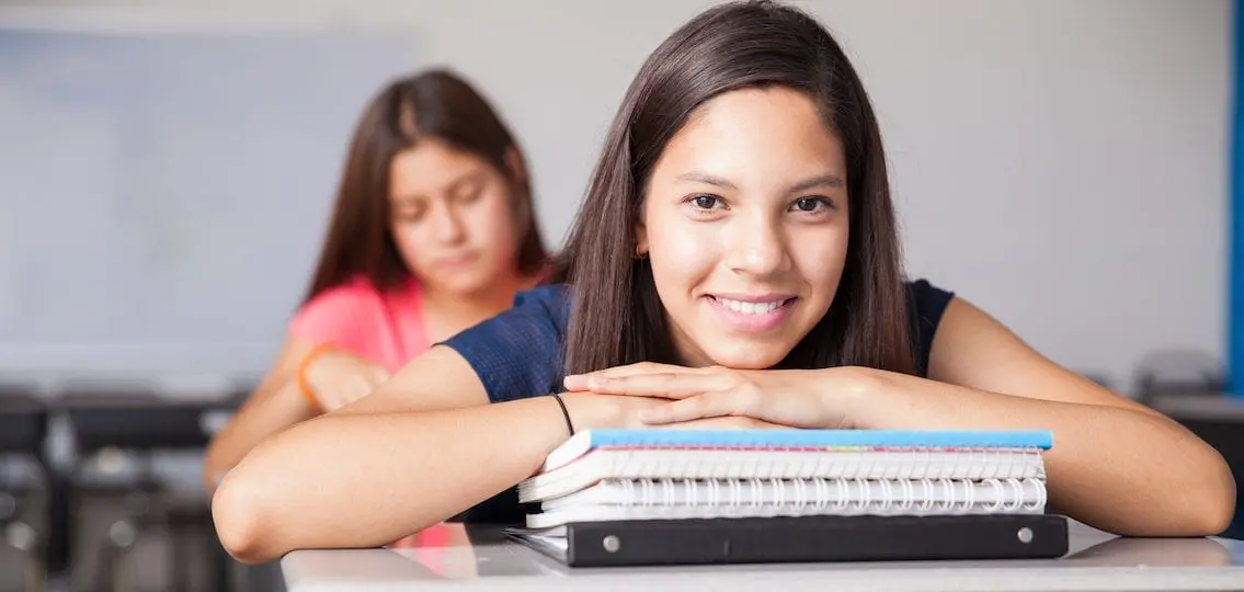 Happy High School Student leaning on spiral notebooks in a classroom