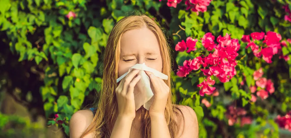 Pollen allergy concept. Young woman is going to sneeze. Flowering trees in background.