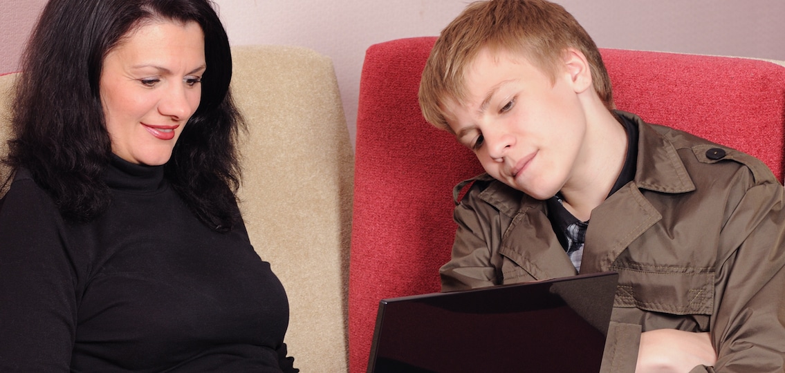 Mother and the son with a laptop sit on a sofa