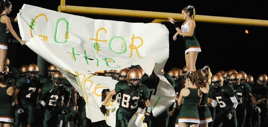 A high school football team and cheerleading squad charging the field