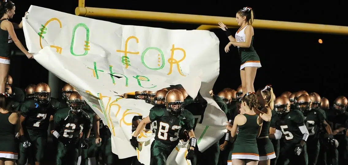 A high school football team and cheerleading squad charging the field