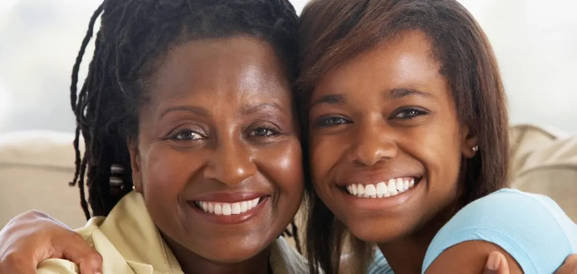 smiling woman hugging her smiling teenage daughter