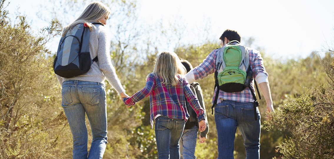 Rear View Of Family Hiking In Countryside Wearing Backpacks