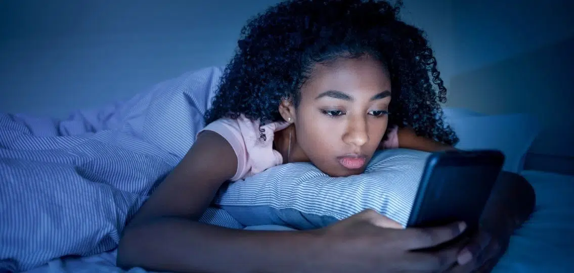 a teenage girl on her cell phone at night in bed looking tired