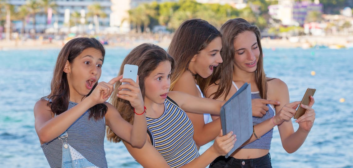 Children playing with Pokemon App game on mobile phones and Ipads on vacation on the beach in Mallorca Spain.