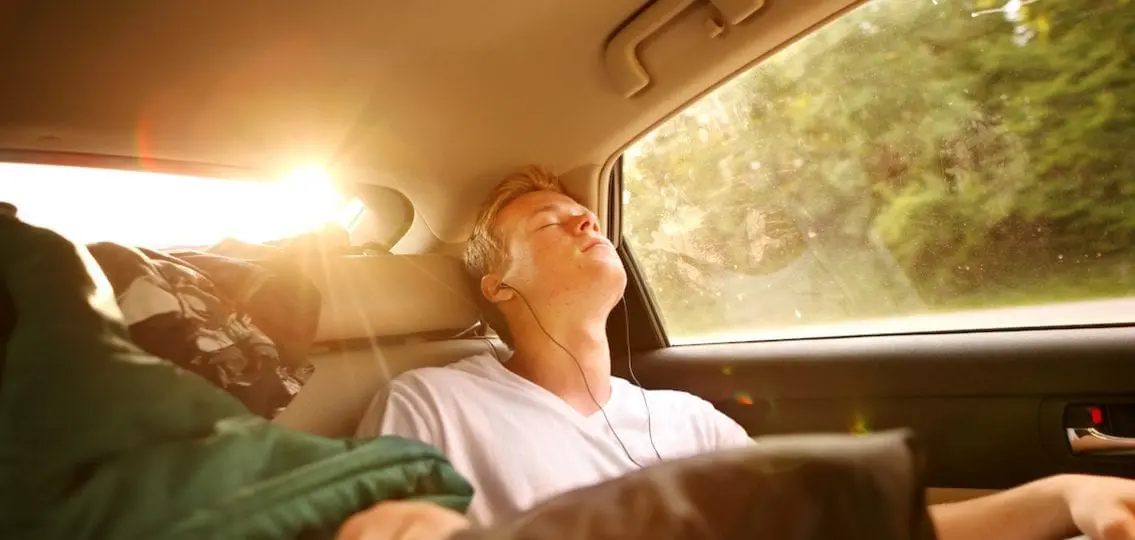 Boy sleeping in back of the car at sunset wearing earplugs