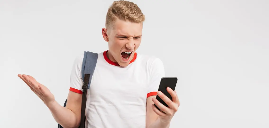 Portrait Of An Angry Teenage Boy Standing With Backpack screaming at phone