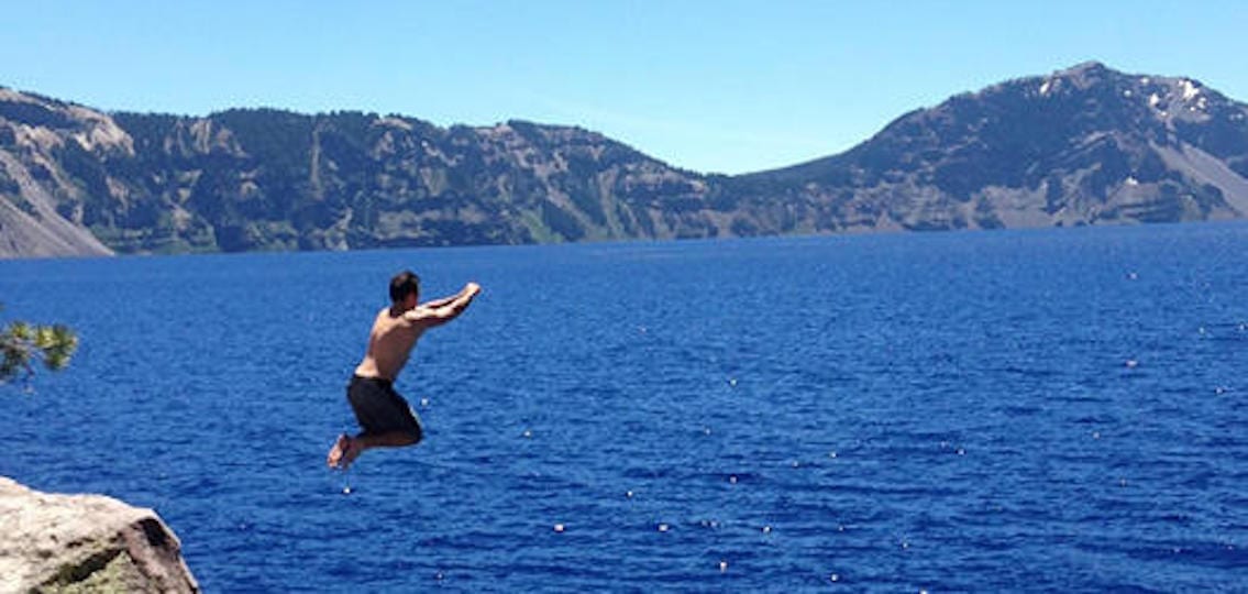 Boy jumping off cliff into crater lake