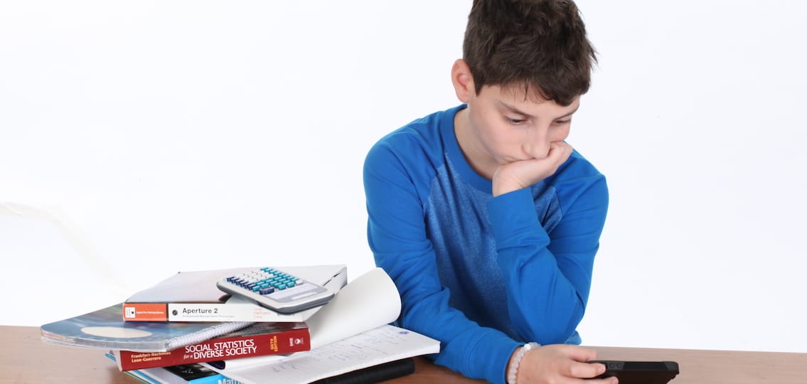 Teen boy with too much homework looking at his phone instead