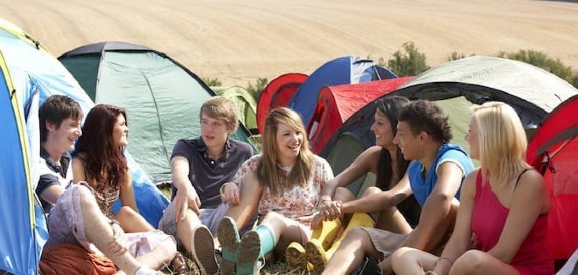 coed teens camping surrounded by tents