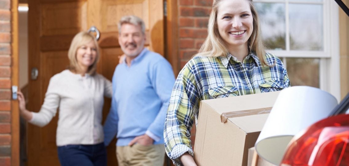 smiling teen girl packing for college putting boxes in the car while her parents smile
