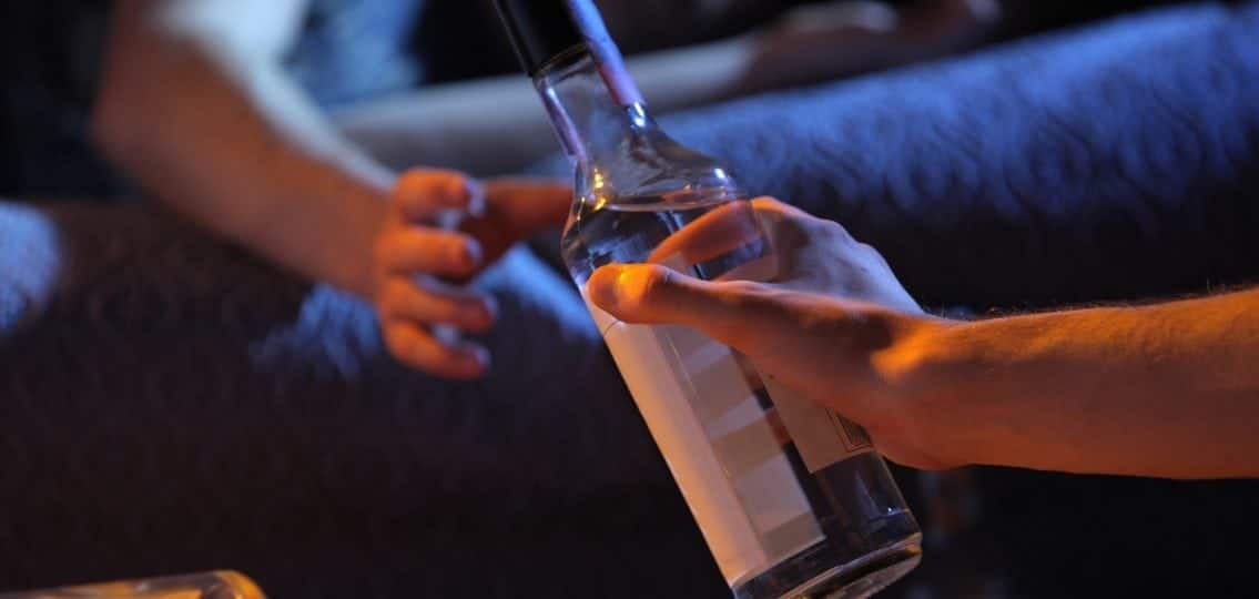 close up of someone passing a bottle of vodka in a dark room