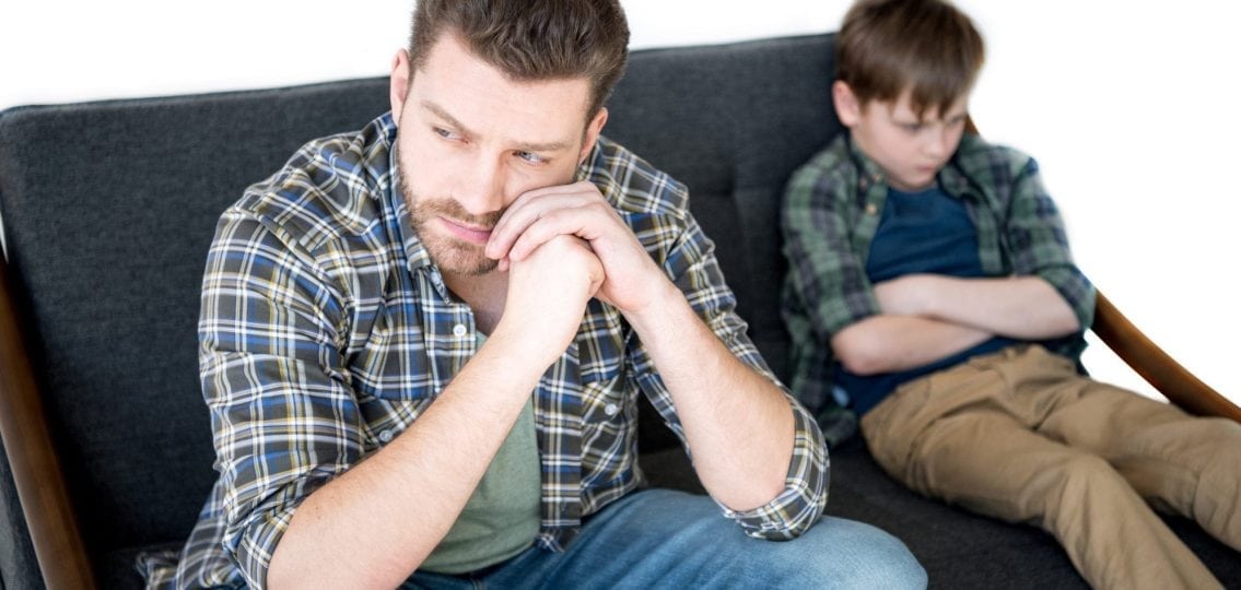 upset dad next to angry tween boy ignoring him on the couch