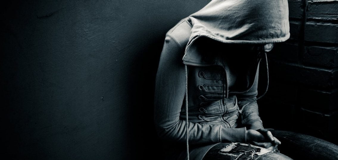 depressed suicidal teenager in a hoodie covering face in black and white