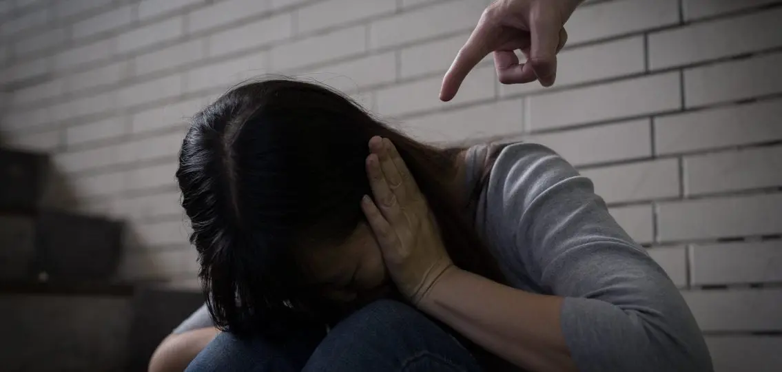 domestic violence abuse victim covering ears while someone stands over her pointing