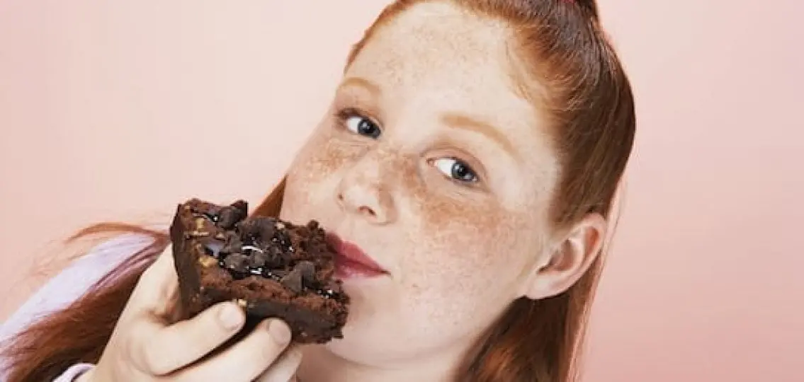 young teen girl eating a brownie and looking into the camera