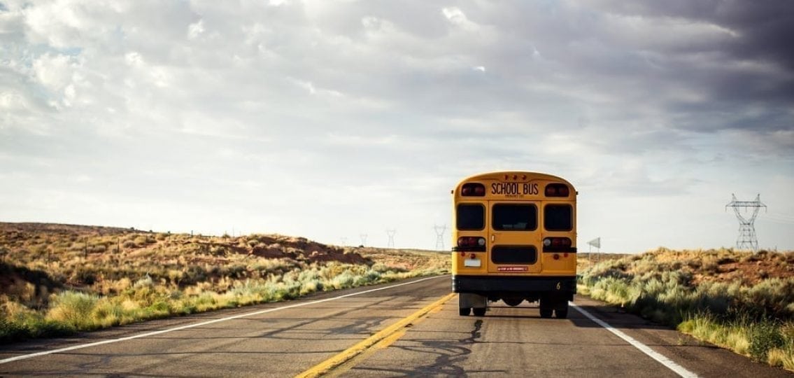 school bus driving away from the camera surrounded by plains
